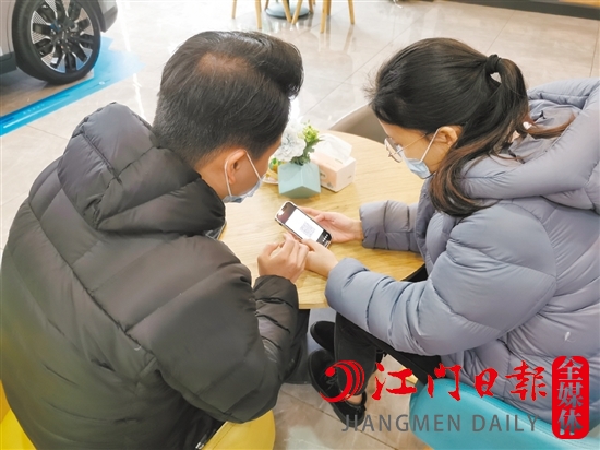 新能源汽車銷售人員協(xié)助車主用手機進行投保新能源汽車險。